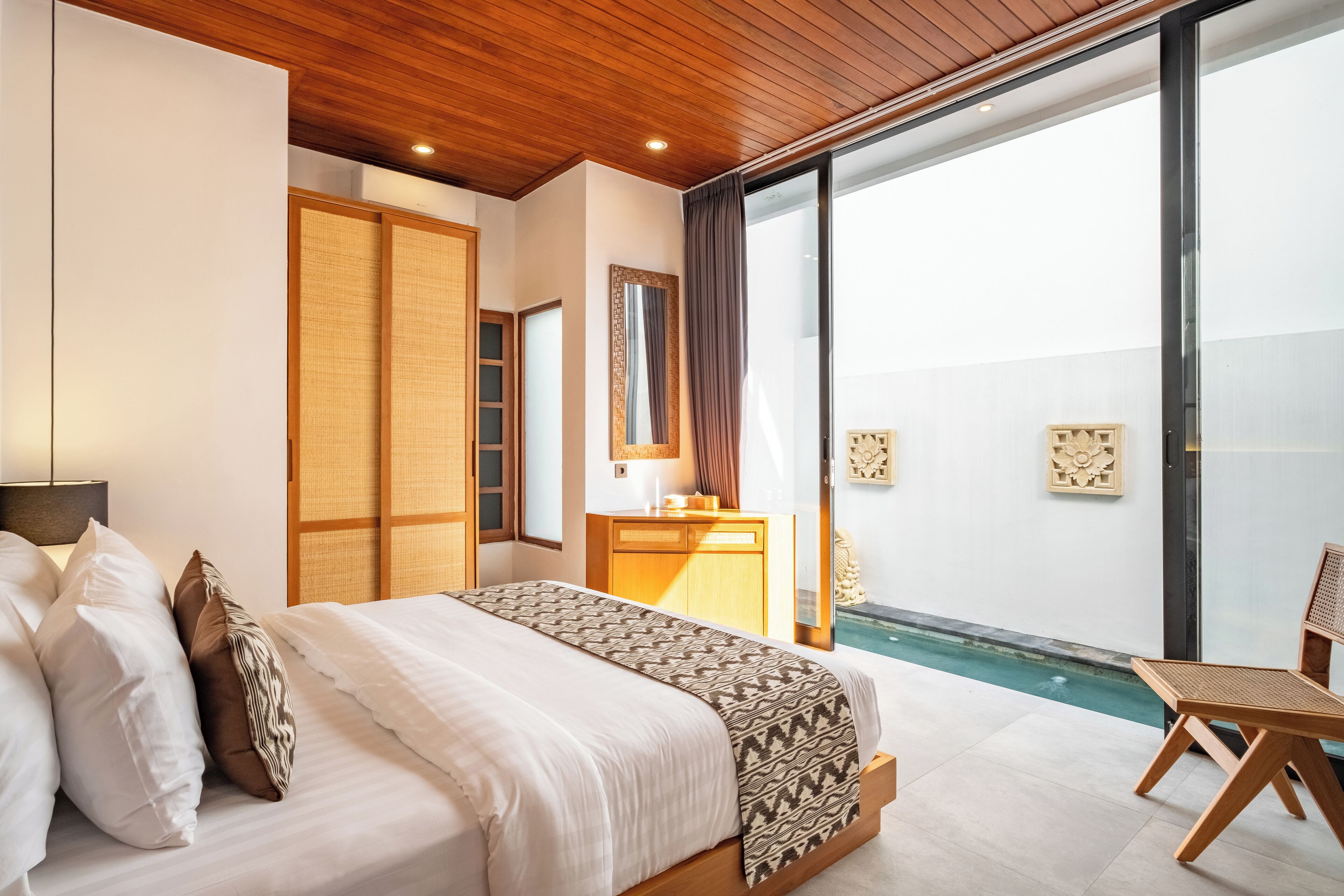 A bedroom with a bed, a nightstand, a mirror, and a view of a swimming pool.