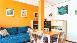Une pièce avec un canapé bleu, une table à manger en bois et des chaises, des murs orange et un sol carrelé.