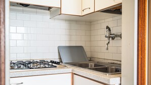 Una cocina con paredes de azulejos blancos, estufa a gas, un lavamanos y armarios de madera.