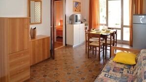 A compact room with a bed, a wooden wardrobe, a dining table with chairs, a kitchenette, and a door leading to another room. - Your perfect home in a peaceful area (Bibione)