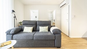 Ein modernes Wohnzimmer mit einem grauen Sofa, einem kleinen runden Tisch und einer Lampe.