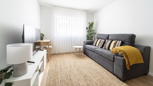 A modern living room with a grey sofa, a small round table, and a TV on a white stand. - Forum Apartments II by House and People (Braga)