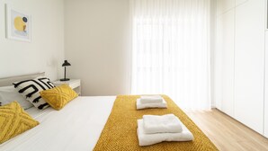 A modern hotel room with a neatly made bed, a bedside table with a lamp, and a large window with sheer curtains. - Forum Apartments II by House and People (Braga)