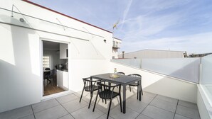 Eine Dachterrasse mit Tisch und Stühlen, einer kleinen Küchenzeile und Blick auf die Stadtlandschaft.
