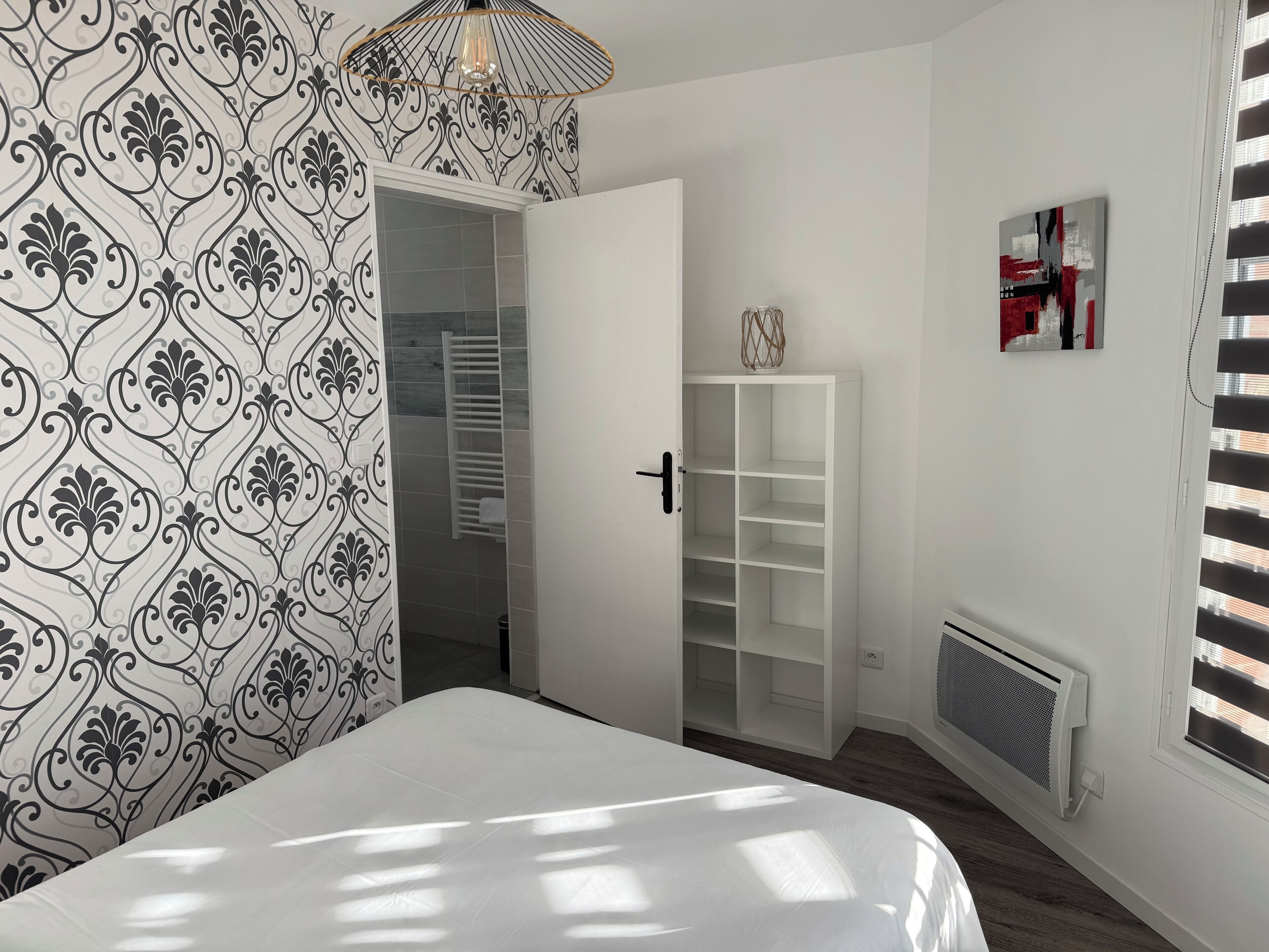 Ein Schlafzimmer mit einem Bett, einem Kleiderschrank, einem Heizkörper und einem Fenster mit Jalousien.