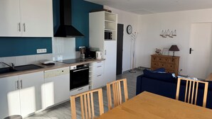 A modern kitchen with white cabinets, a black range hood, and a wooden dining table with chairs. - Grain de Café Barneville Plage (Barneville-Carteret)