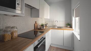 A compact kitchen with a microwave, oven, and sink. There are jars of pasta on the counter and a plant on the windowsill.