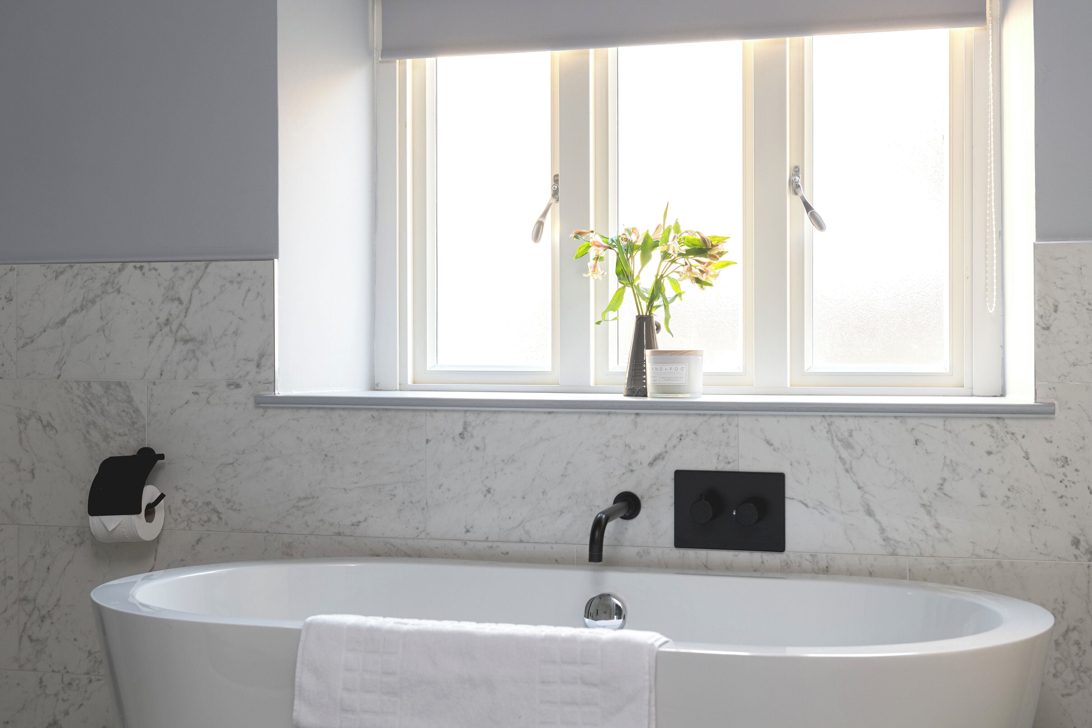 A modern bathroom with a freestanding bathtub, a window with a potted plant, and a towel rack.