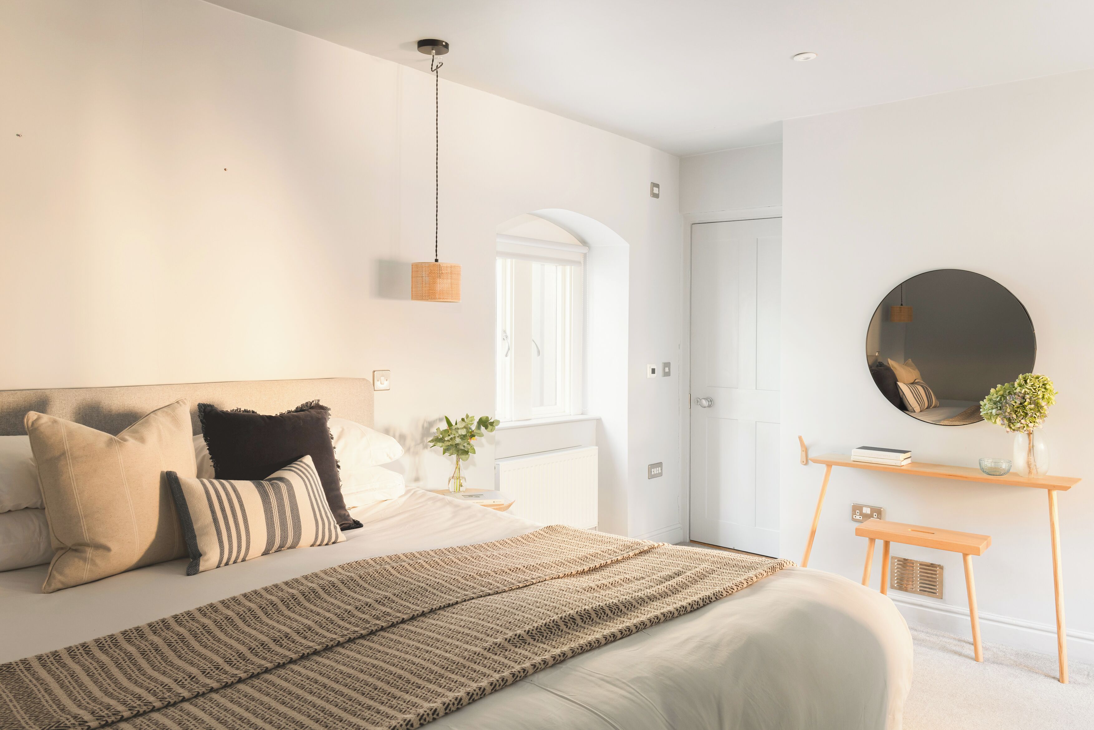 A modern bedroom with a bed, bedside table, and a round mirror on the wall.