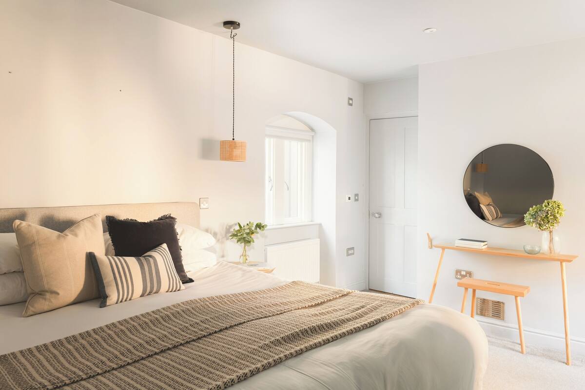 A modern bedroom with a bed, bedside table, and a round mirror on the wall.