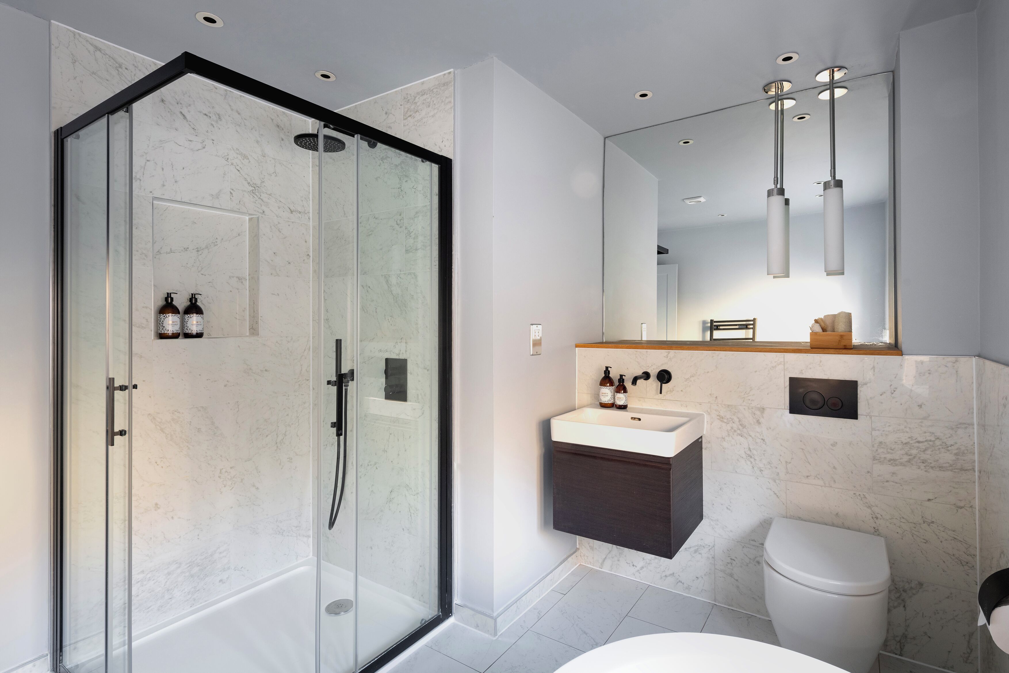 A modern bathroom with a glass-enclosed shower, a white sink with dark cabinetry, and a toilet.