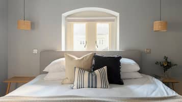 Un lit bien fait, recouvert d’une couvre-lit à motifs, une fenêtre donnant sur des immeubles et deux lampes en osier suspendues.