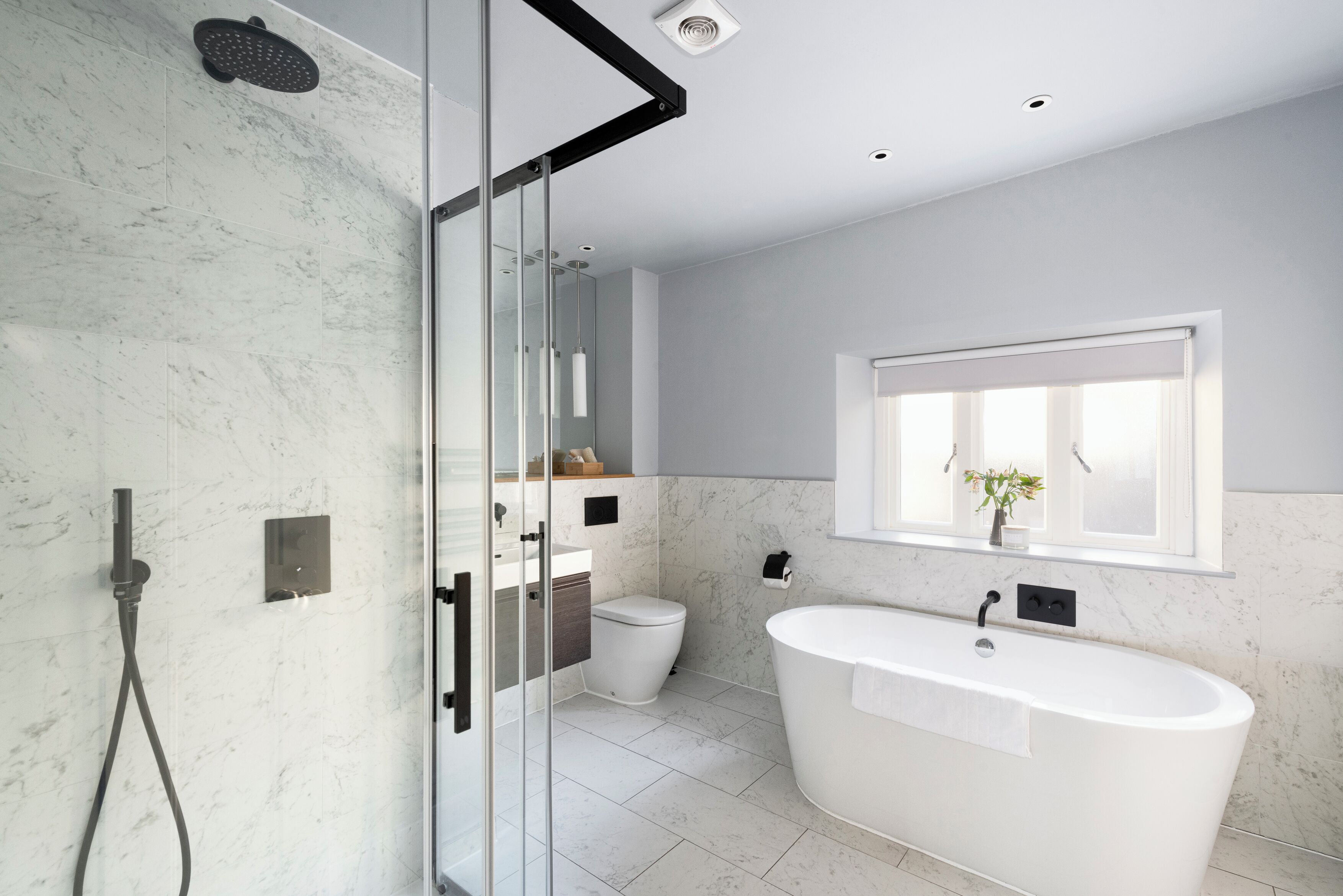 A modern bathroom with a glass shower enclosure, a freestanding bathtub, and a toilet.