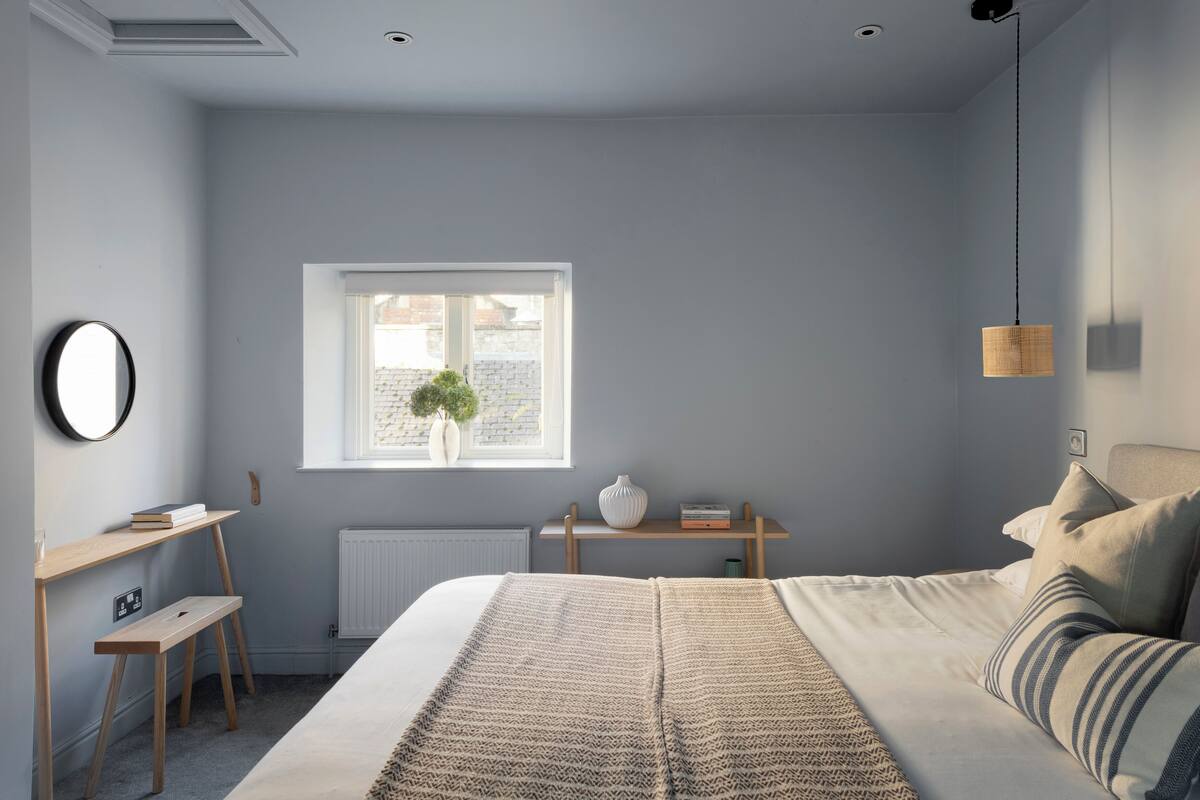 A bedroom with a bed, bedside table, and a window with a view of buildings.