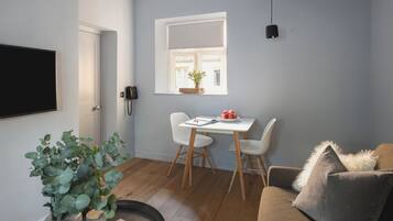 Een moderne woonkamer met een eetgedeelte, een televisie en een raam met uitzicht op een gebouw.