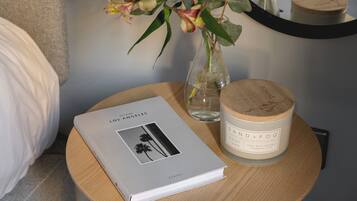 A book titled "Los Angeles" on a round wooden table, a candle with a wooden lid, and a vase with flowers.