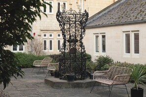 A courtyard with a wrought iron fountain, wicker chairs, and potted plants. - St Catherine's Hospital - Bath (Bath)