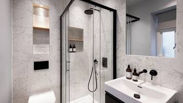 A modern bathroom with a glass-enclosed shower, a white sink, and a toilet.