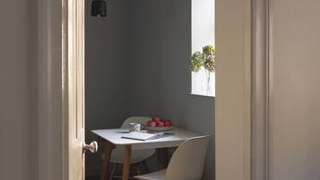 Un comedor con una mesa, sillas, un bol de fruta, un libro y un florero con flores.