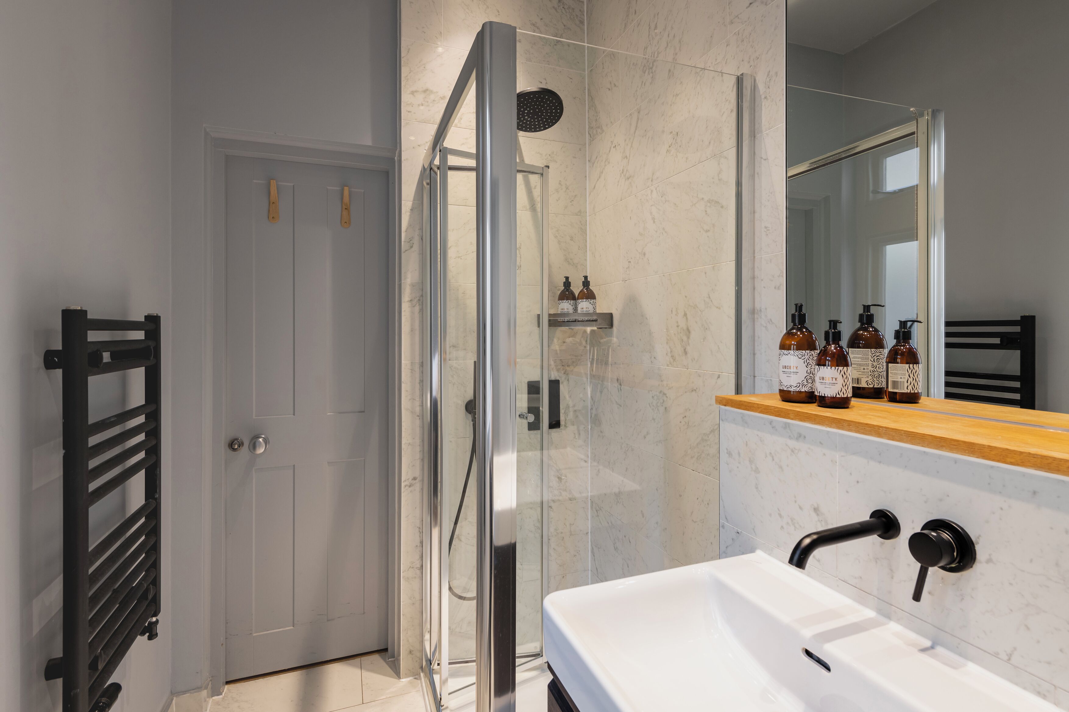 Un baño moderno con ducha de vidrio, lavamanos blanco con grifo negro y encimera de madera sobre el lavamanos.