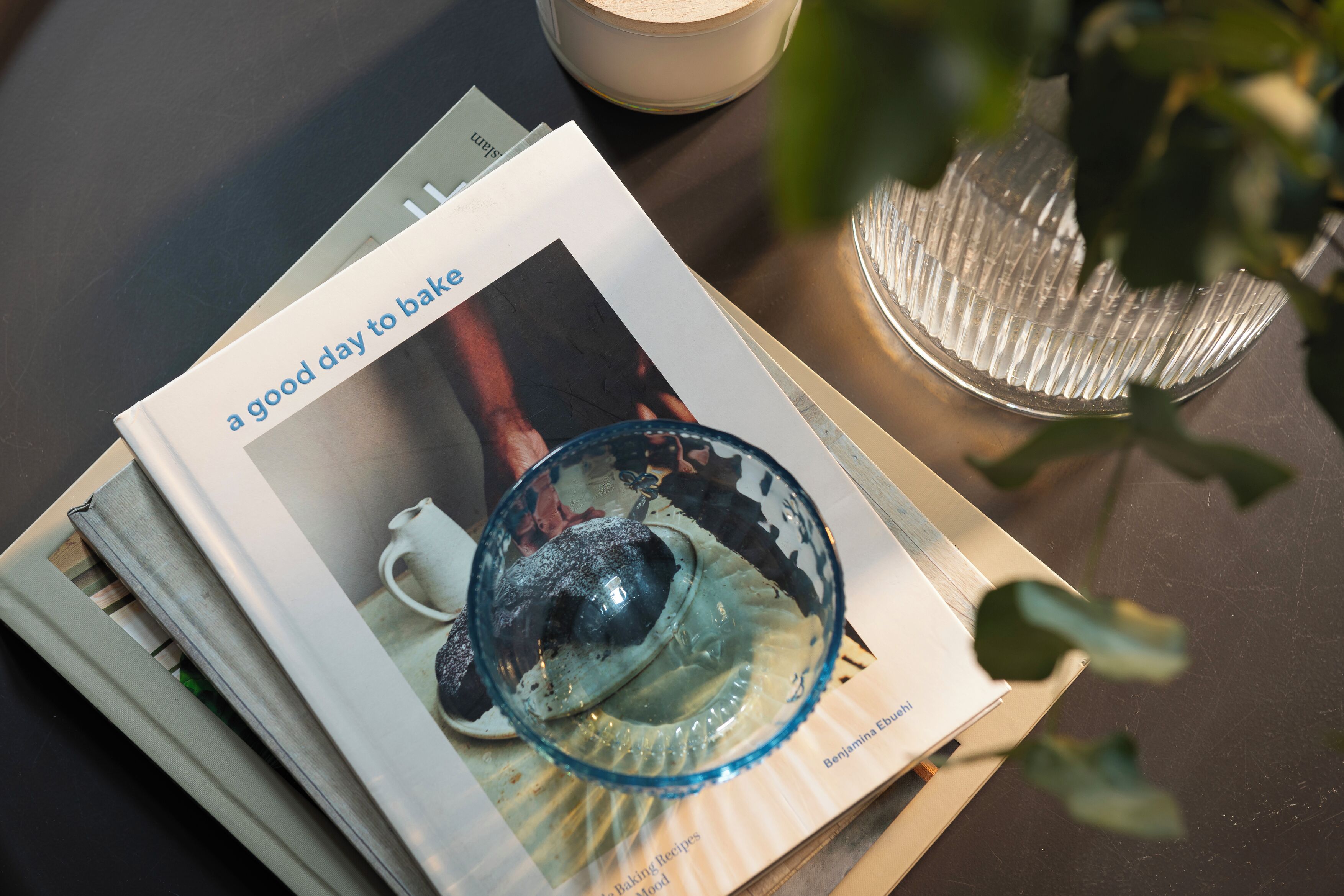 A book titled "a good day to bake" on a table with a glass and a candle.