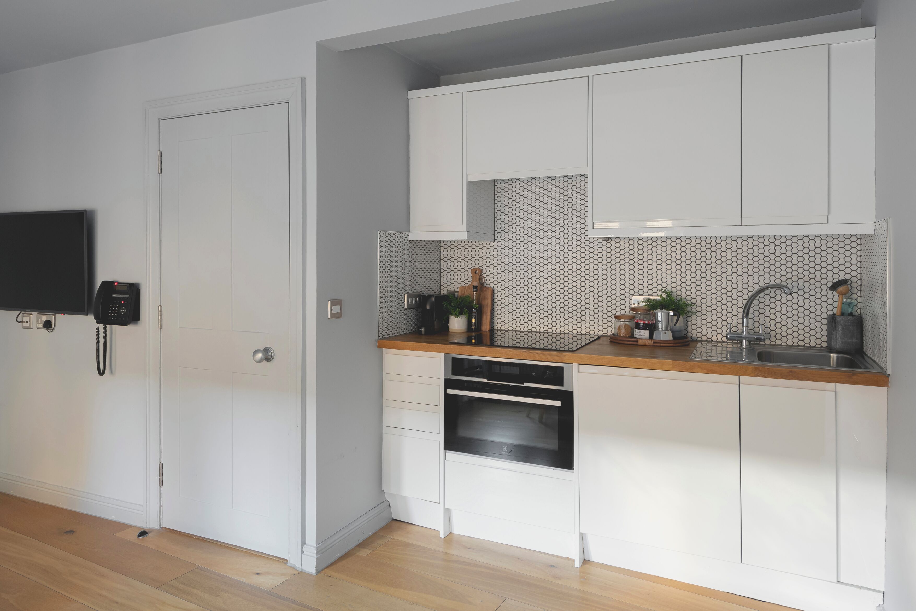 Eine moderne Küche mit weißen Schränken, einer Holz Arbeitsplatte, einem eingebauten Ofen und einer gefliesten Spritzschutzwand.
