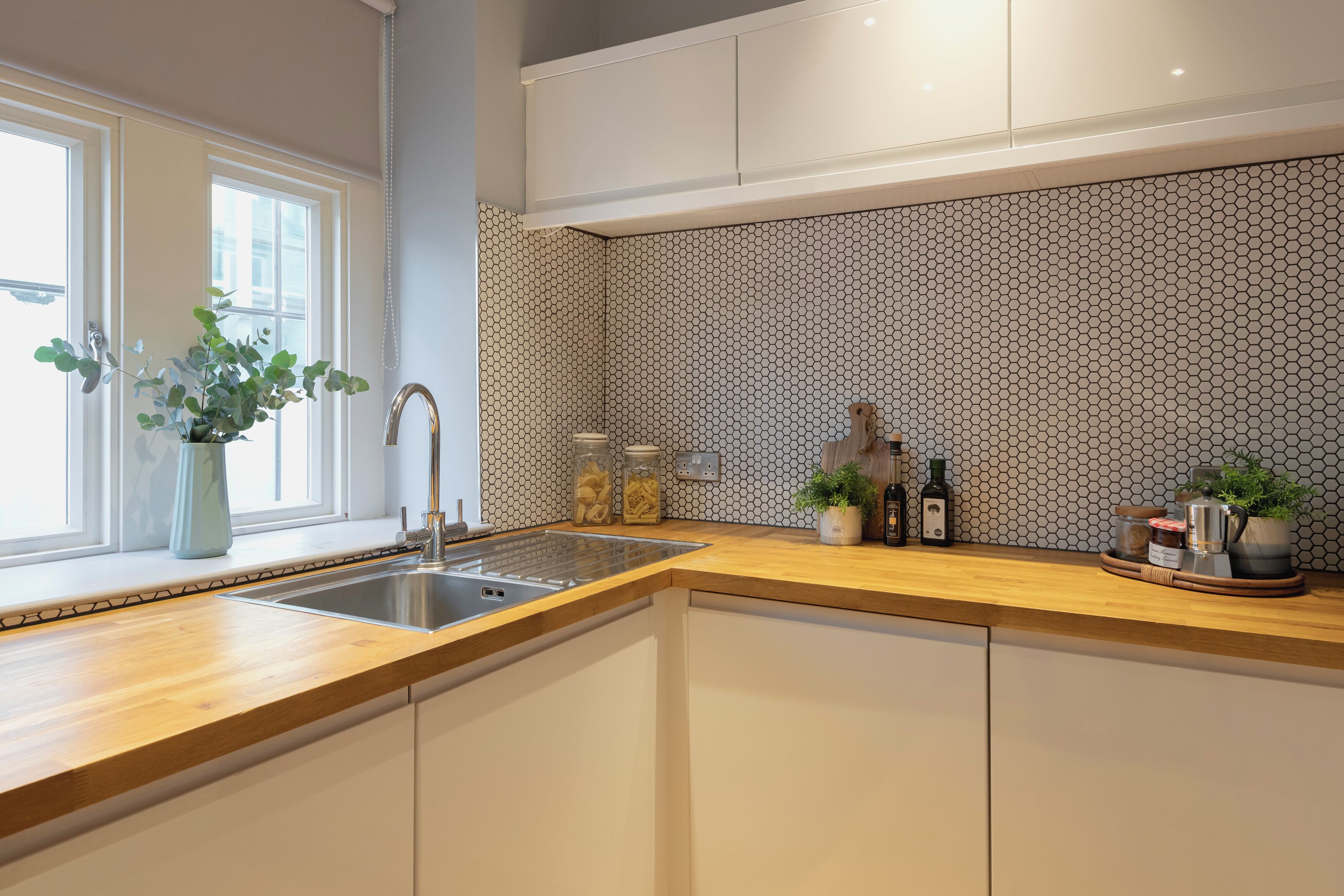 A modern kitchen with a wooden countertop, a stainless steel sink, and a hexagonal patterned backsplash.