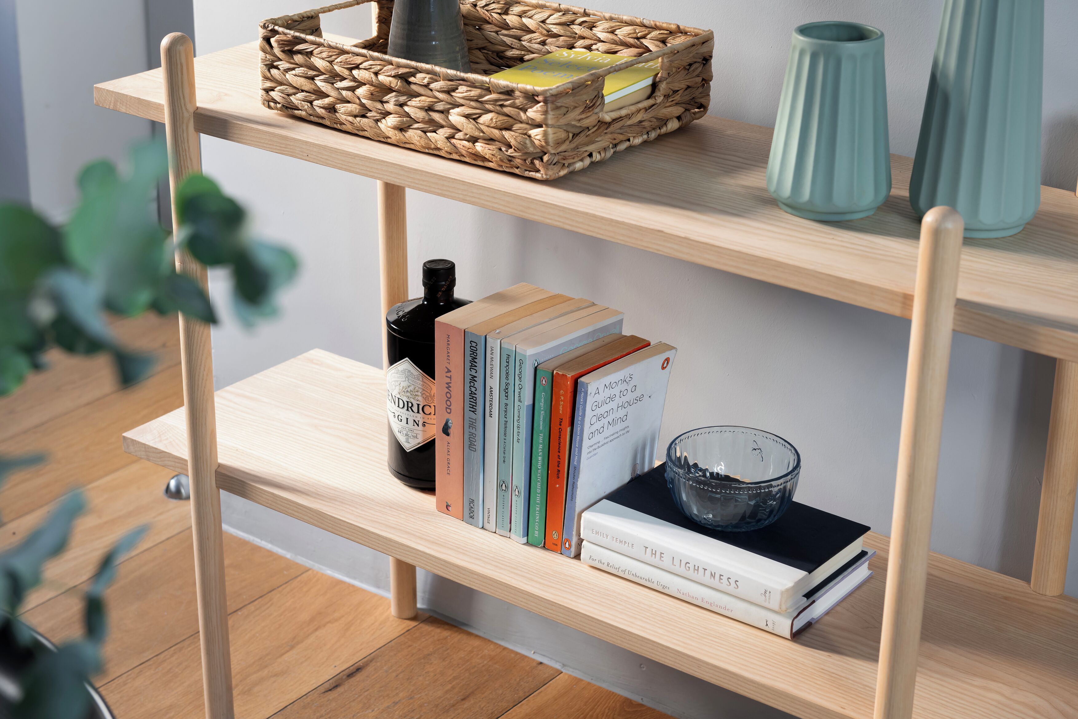 Uma prateleira de madeira com uma cesta trançada, livros, uma garrafa e vasos decorativos.