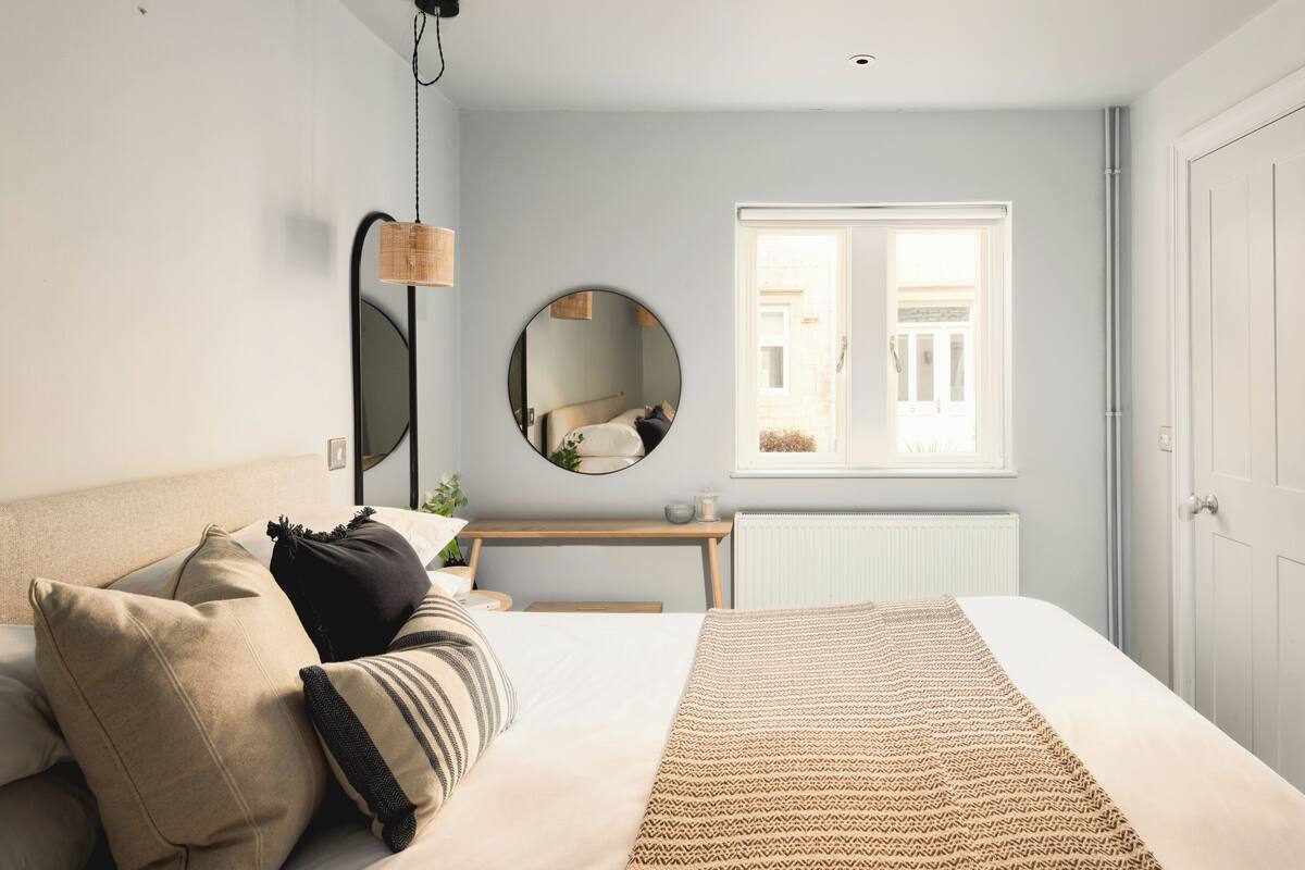 A bedroom with a bed, bedside table, mirror, window, and radiator.