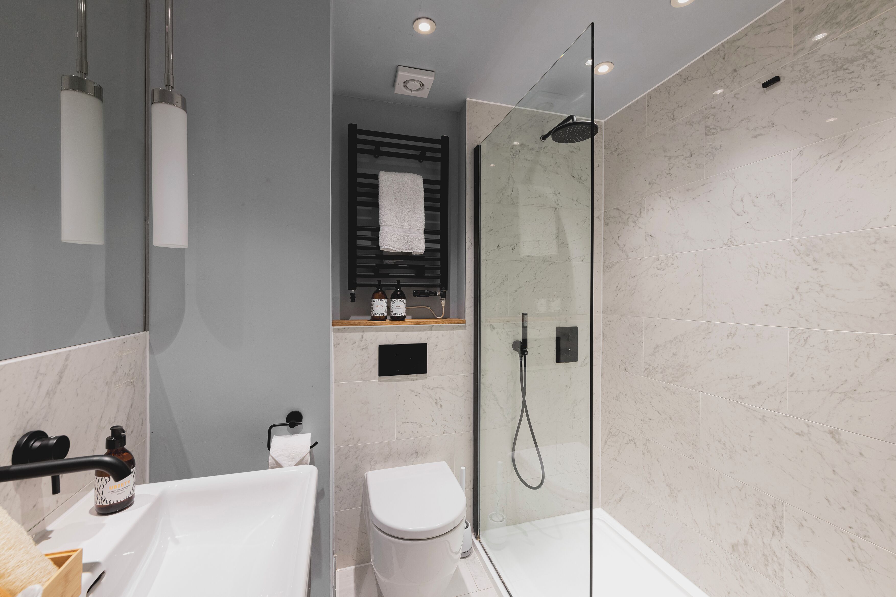 A modern bathroom with a glass-enclosed shower, a white bathtub, and a toilet.