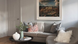 A living room with a grey sofa, a white vase, and a framed picture of a desert landscape on the wall. - St Catherine's Hospital - Bath (Bath)