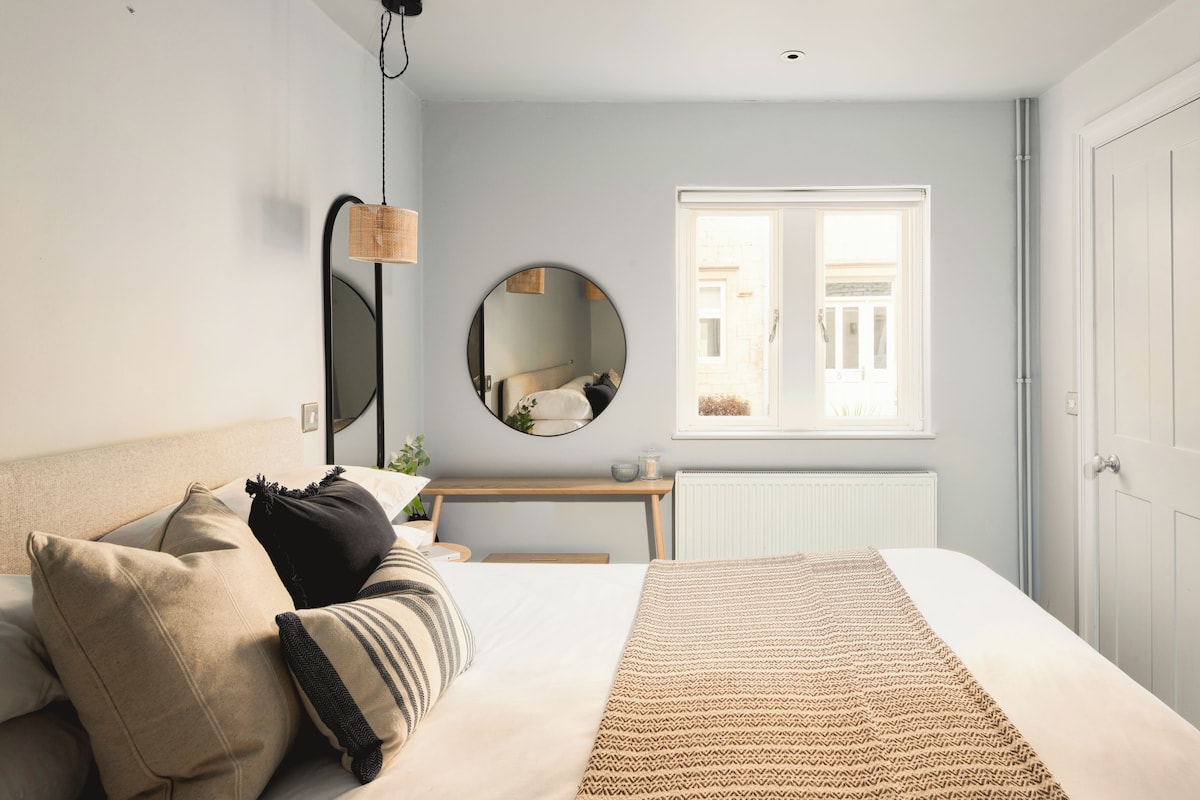 A bedroom with a bed, bedside table, mirror, window, and radiator.