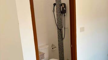 Un pasillo estrecho que conduce a un baño con inodoro, ducha y un pequeño ventanal.