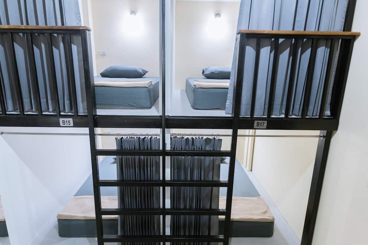 A dormitory-style room with bunk beds, a small seating area, and a window with curtains.