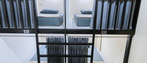 Une chambre de type dortoir, avec des lits superposés, un petit coin salon et une fenêtre avec des rideaux.