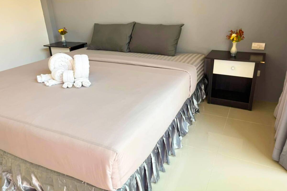 A neatly made bed with a pink bedspread, two pillows, and a small table with a vase of flowers.