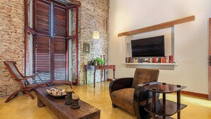 A cozy living room with a stone wall, wooden furniture, a television, and a bookshelf. - Casa Palos - 5 BR Downtown Luxury House (Cartagena de Indias)