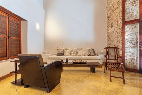 A living room with a sofa, a wooden chair, a coffee table, and a stone wall.