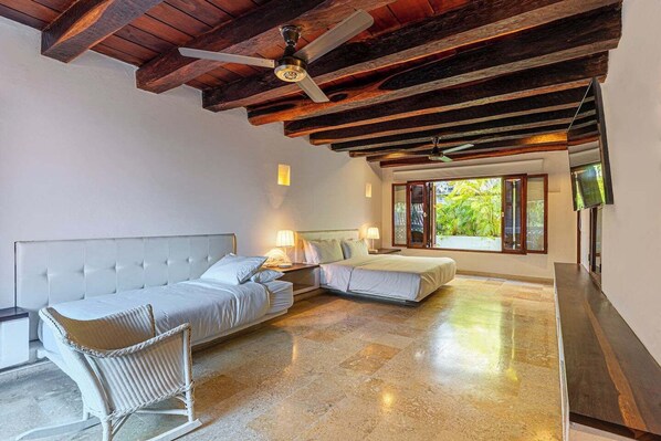 Une chambre à coucher avec un grand lit, un plus petit lit, une chaise et un ventilateur de plafond.