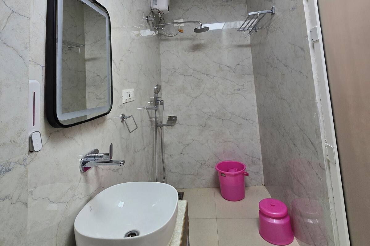 Casa de banho com lavatório branco, espelho, chuveiro e sanita.