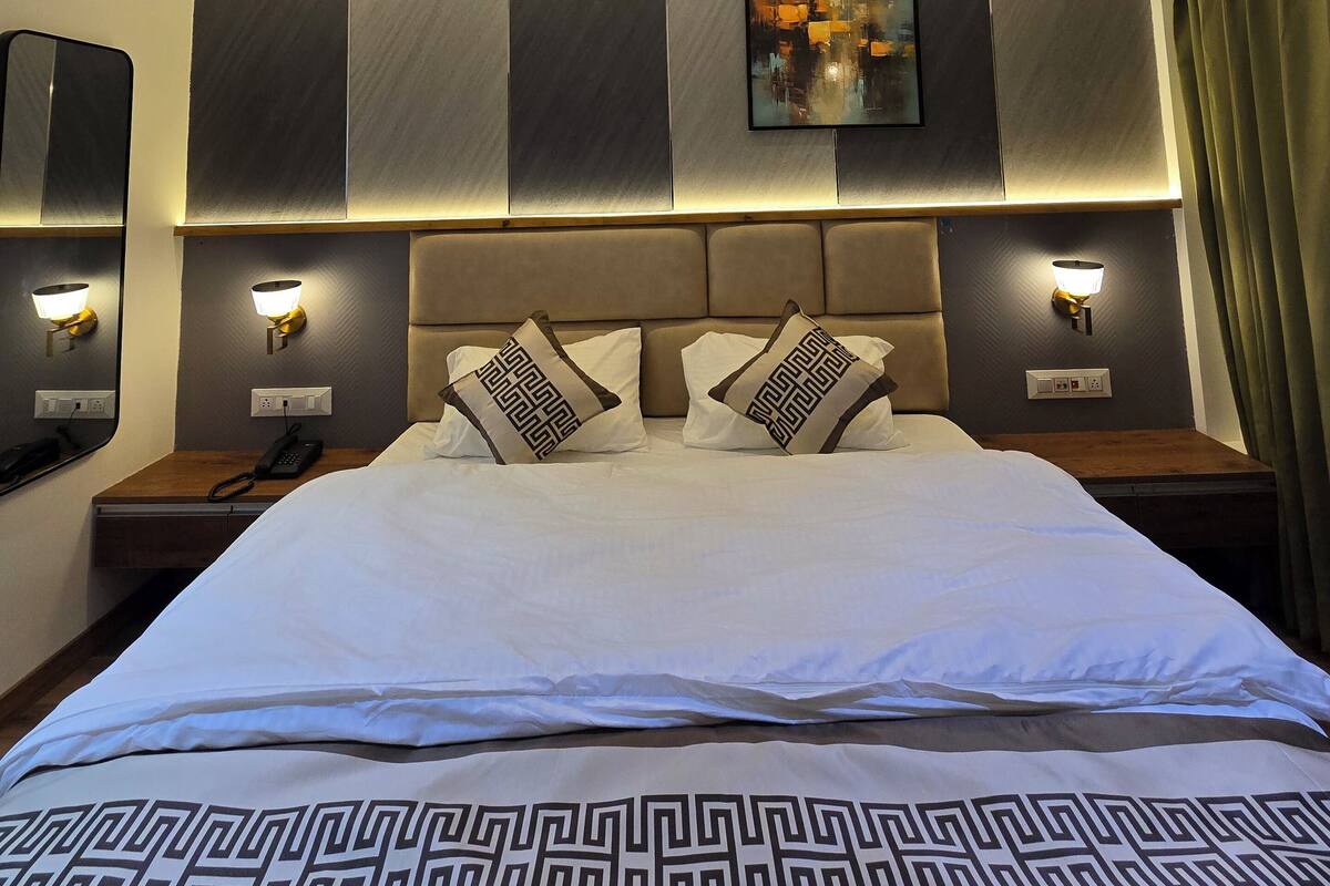 Quarto de hotel moderno com uma cama grande, cabeceira com iluminação integrada, um quadro sobre a cama e uma mesa de cabeceira com telefone.