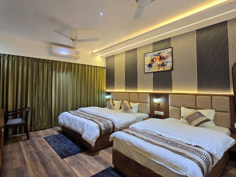 Habitación de hotel con dos camas, ventilador de techo, aire acondicionado, una silla de madera y un cuadro grande en la pared.