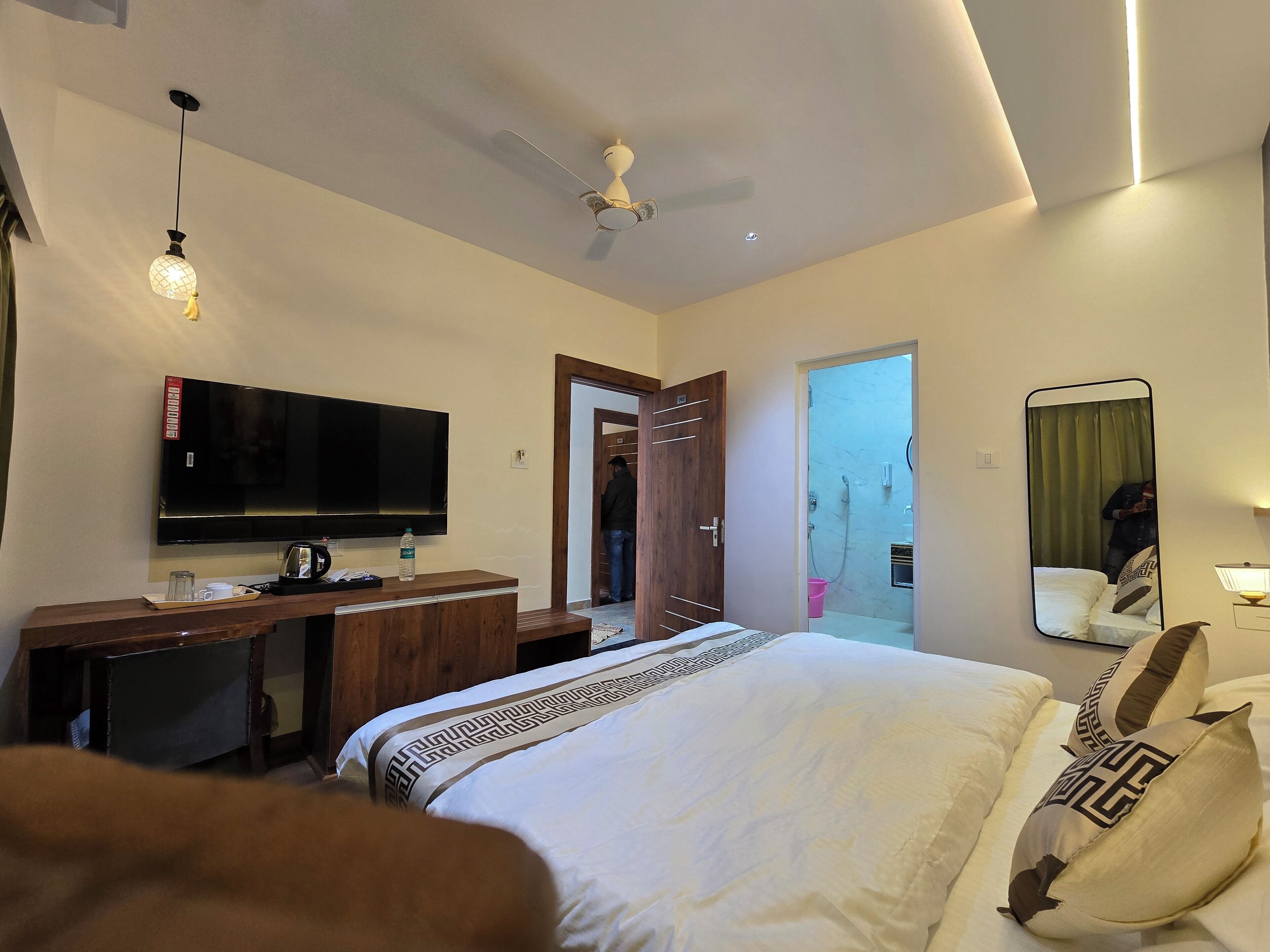 Une chambre d’hôtel moderne dotée d’un grand lit, d’une télévision, d’un bureau avec une bouteille d’eau et d’un ventilateur de plafond.