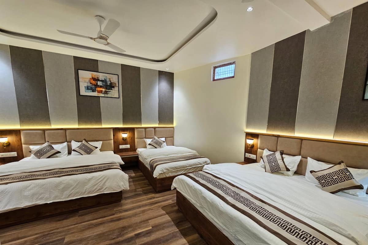 Quarto de hotel com três camas, ventilador de teto e uma janela pequena.