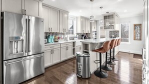 A modern kitchen with stainless steel appliances, white cabinetry, and a bar area with stools. - Spacious 5-bedroom house in lovely Arlington with AC, WiFi (Arlington)