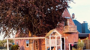 A brick house with a large tree, a swing set, and a small wooden playhouse. - Hus Heideblick between nature and the North Sea (Sankt Michaelisdonn)