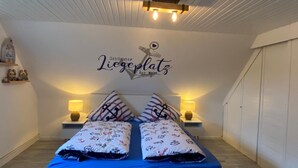 A bedroom with a bed, two bedside lamps, a wall decoration, and a ceiling light fixture. - Hus Heideblick between nature and the North Sea (Sankt Michaelisdonn)