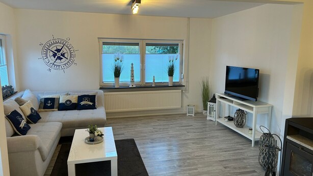 A modern living room with a white sofa, a coffee table, a TV, and a fireplace. - Hus Heideblick between nature and the North Sea (Sankt Michaelisdonn)
