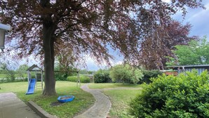 A residential backyard with a paved path, a blue slide, and a small garden area. - Hus Heideblick between nature and the North Sea (Sankt Michaelisdonn)