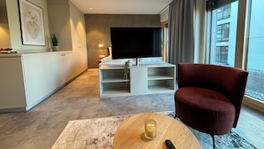 Una sala de estar moderna con una televisión, una silla roja, una mesa de centro de madera y un control remoto.